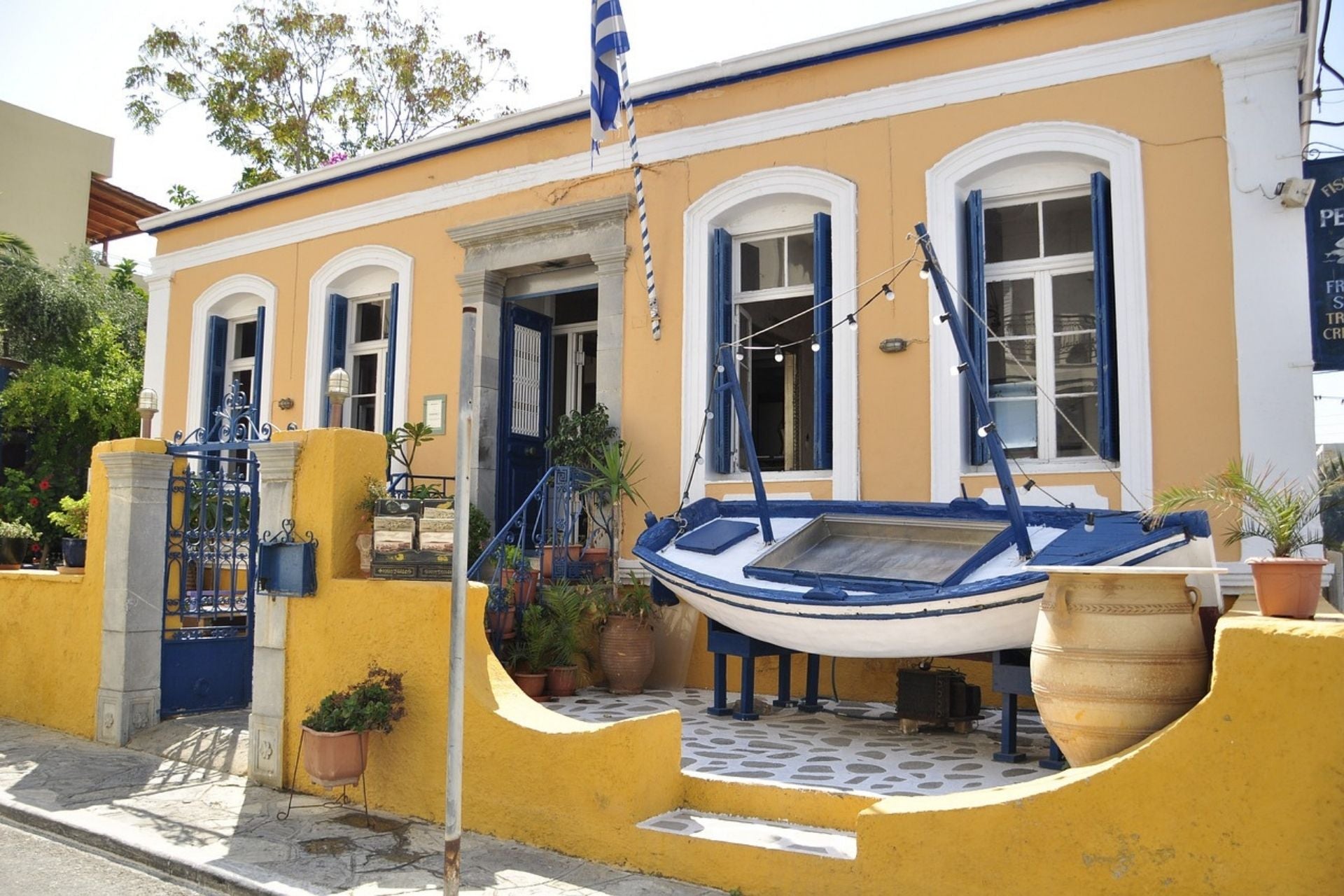 Geel huis met blauwe luiken en een zeilboot in de tuin