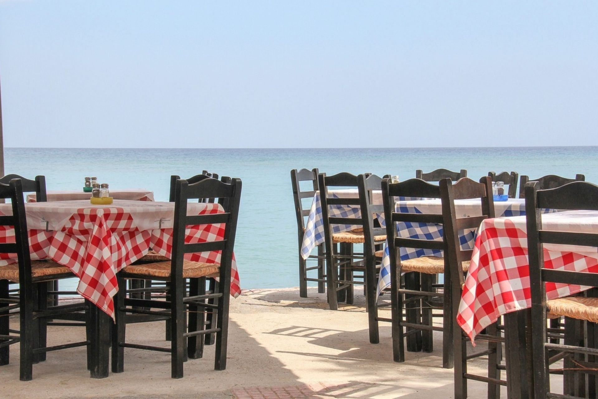 Restaurant aan zee met bruine houten stoelen en geblokte tafelkleedjes