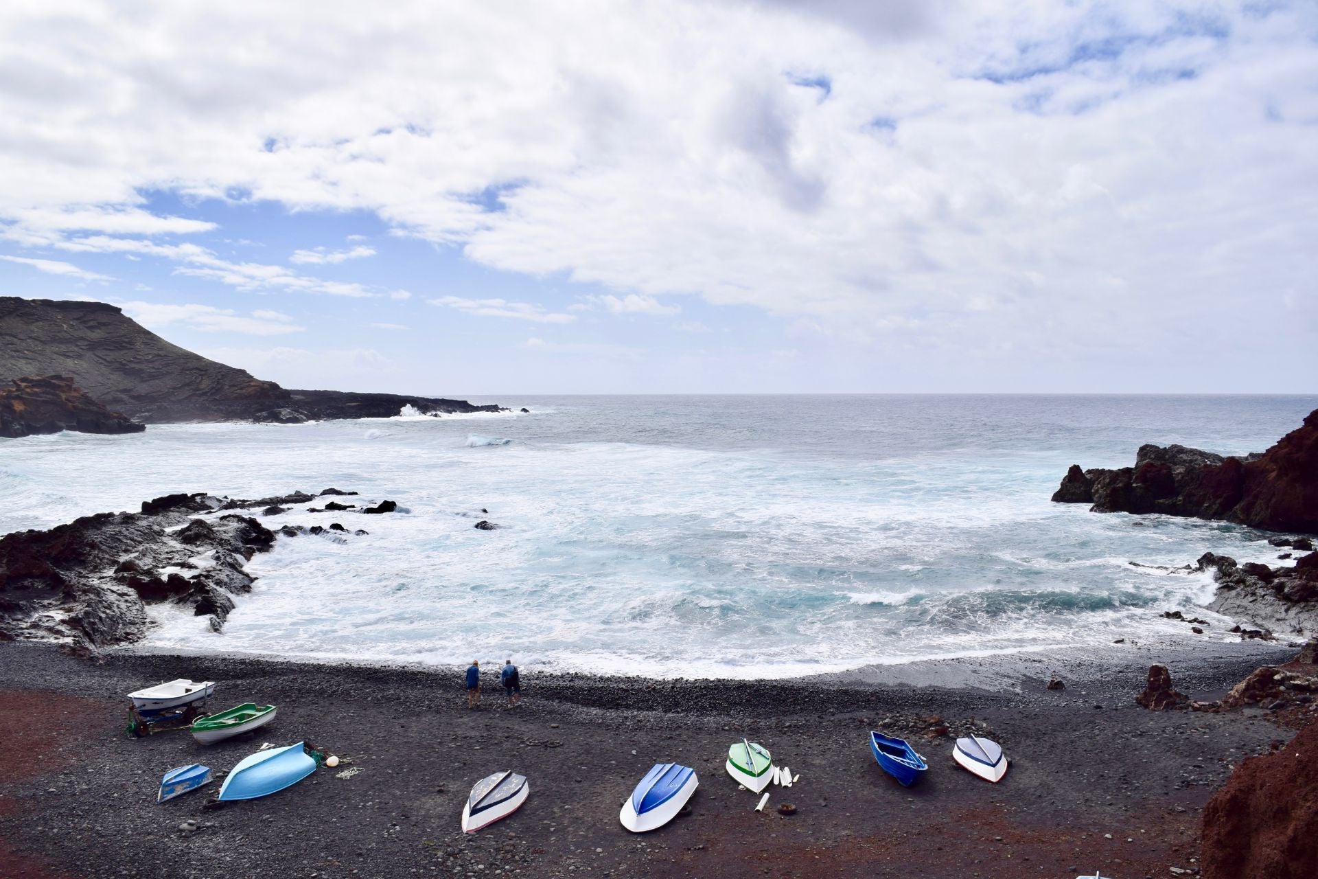 Baai met zwart lavastrand met gekleurde bootjes en wilde golven